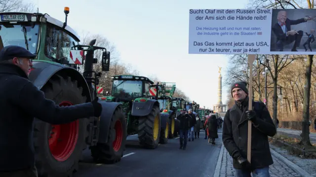 A man walking with a sign beside tractors