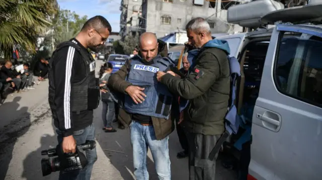 Two men help a journalist put on a press vest in Rafah, in Gaza, on 14 January