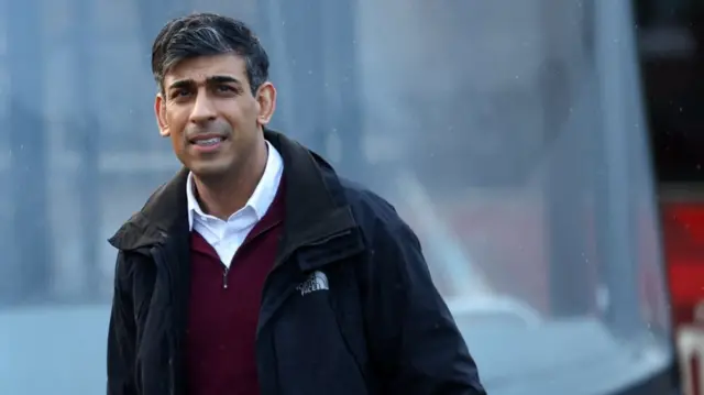 Rishi Sunak walks near a bus, wearing a black jacket