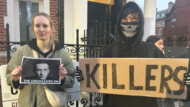 Erika Kirichenko and a man stand outside the Russian embassy in London holding up signs mourning the death of Alexei Navalny, with one sign reading: 'the dream lives on'