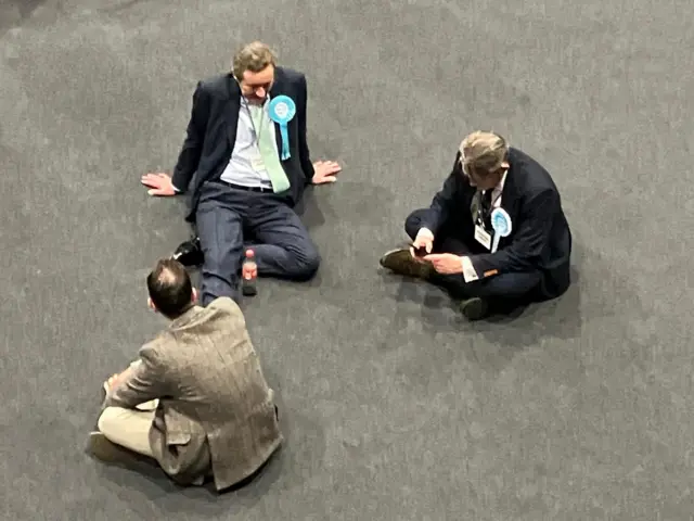 Three men sat on the floor at the election count in Wellingborough.