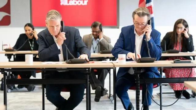 Labour leader Sir Keir Starmer sits with musician Feargal Sharkey while phone canvassing in the Wellingborough and Kingswood by-elections.