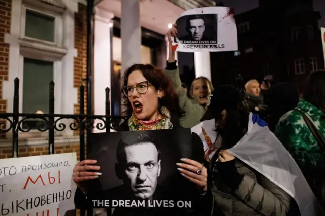 A woman holds a placard bearing Navalny's face that says 'the dream lives on' outside the Russian Embassy in London