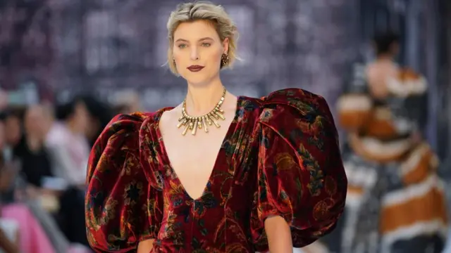 A model walks the catwalk at the Paul Costelloe show wearing a red, velvet dress with puffy sleeves