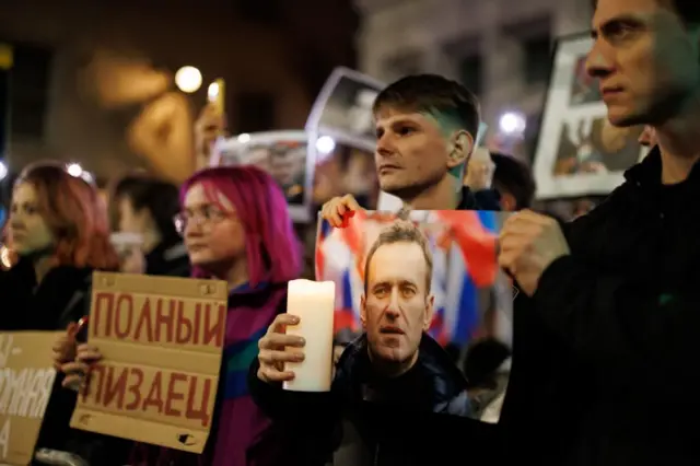 Men and women in a line holding candles, placards in Russian and images of Alexei Navalny