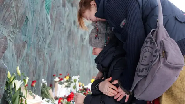 Two women embrace as they lay flowers at the Wall of Grief monument