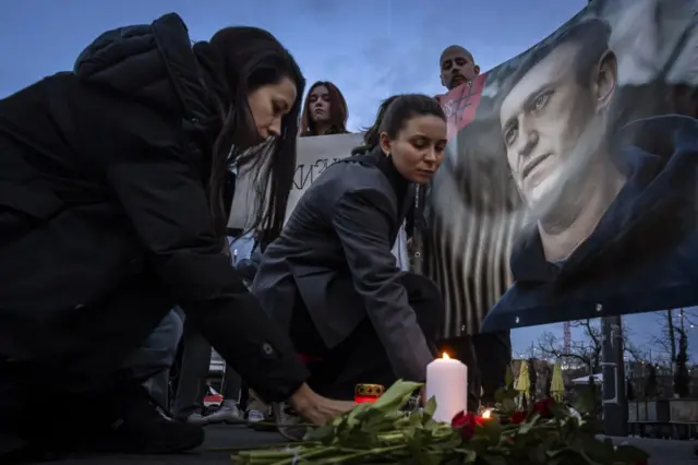 Two women lay down flowers and candles next to a portrait of Russian opposition leader Alexey Navalny