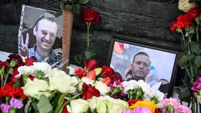 Photographs showing late Russian opposition leader Alexei Navalnyare are displayed next to flowers at the monument to the victims of political repressions in Moscow