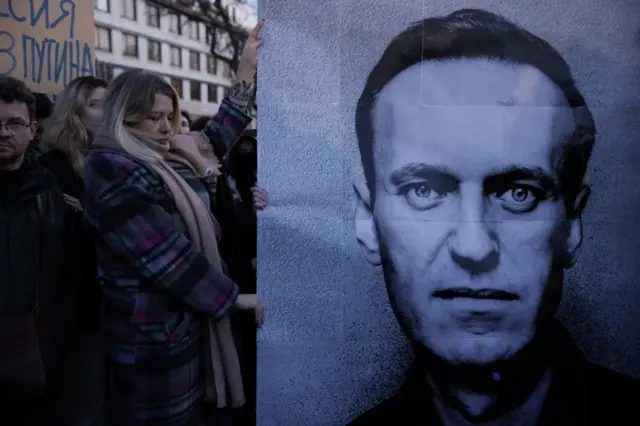 People gather outside the Russian embassy in Warsaw, Poland holding up large poster of Alexei Navalny