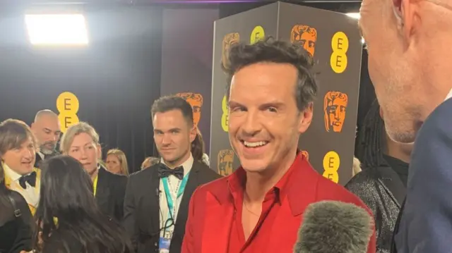 Andrew Scott, dressed in a red shirt and suit, on the red carpet