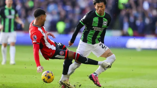 Sheffield United's Mason Holgate catches Kaoru Mitoma just below the Brighton player's knee