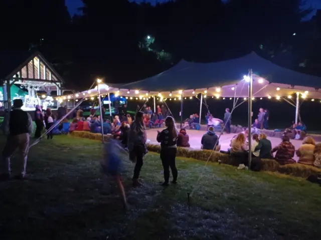 People gathered in a tent lit by fairy lights at Equinox Festival