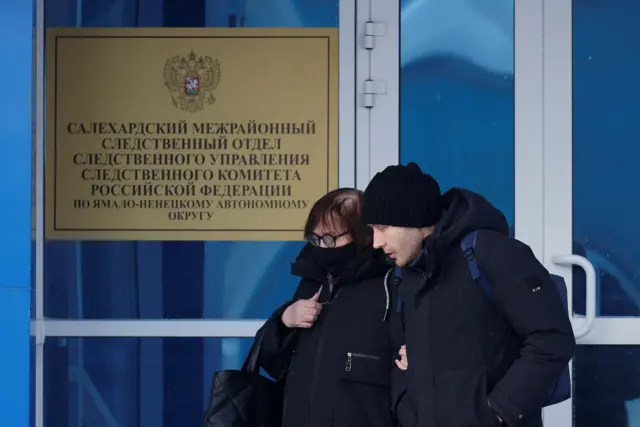 A man and woman wearing a coat and beanie walking out of a building.