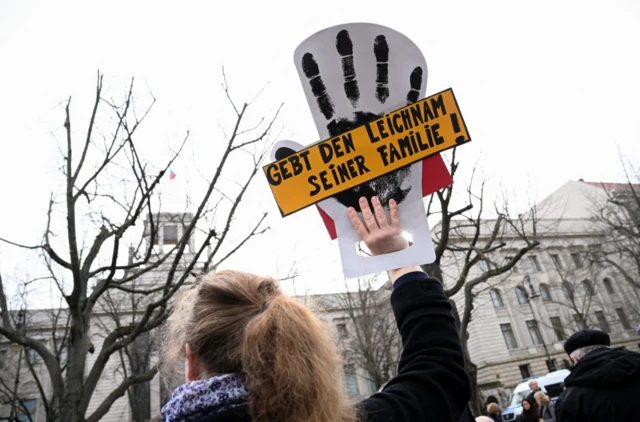 A woman holds a placard outside Russia's embassy in Berlin which translates to 'give the body to his family'