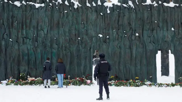 A police officer stands guard as people lay flowers at the Wall of Grief monument to the victims of political repressions to honour the memory of Russian opposition leader Alexei Navalny in Moscow