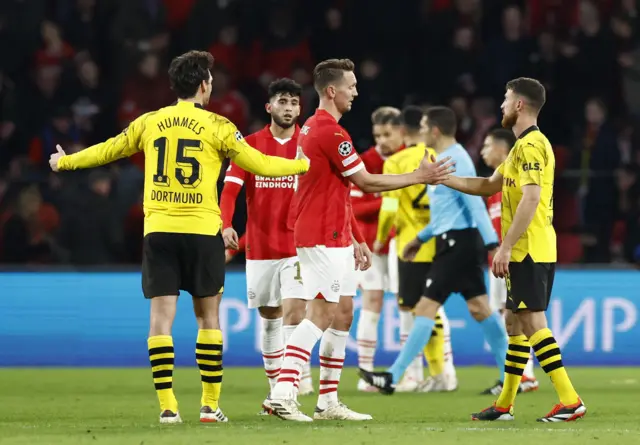 PSV and Dortmund players shake hands at full time on the pitch.