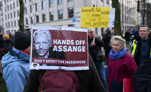 A sign, displayed on the back of a person in a crowd, reads: Don't shoot the messenger