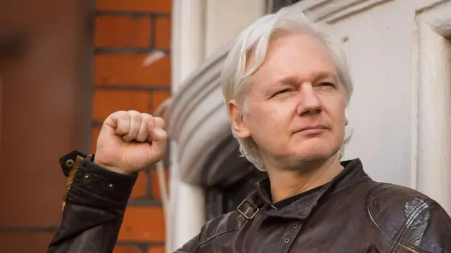 Julian Assange speaks from the balcony of the Ecuadorian embassy in London with his fist raised in the air