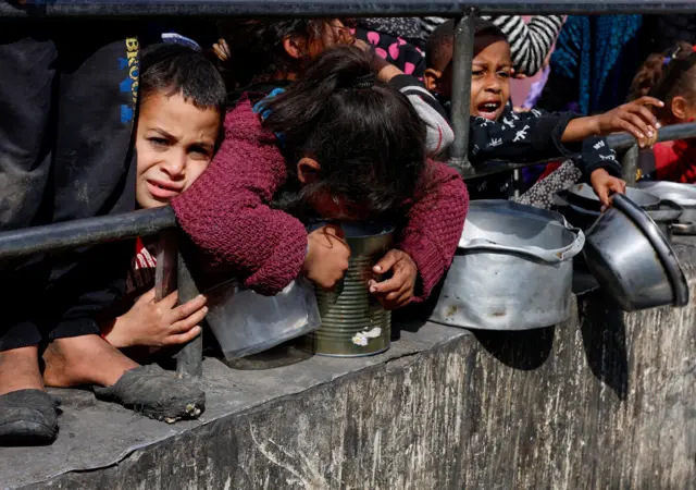 Children wait with pans to collect food