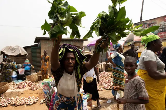 A woman raises up vegetables during a demonstration against the hike in price and hard living conditions in Ibadan on February 19, 2024.