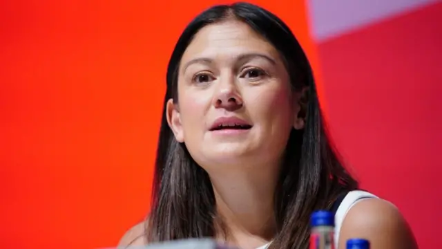 Lisa Nandy sits on a panel in front of a red backdrop at a Labour conference