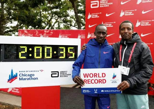 Kenya's Kelvin Kiptum poses with his coach Rwandan Gervais Hakizimana (R) next to the clock marking Kiptum's time after winning the 2023 Bank of America Chicago Marathon in Chicago, Illinois, in a world record time of two hours and 35 seconds on October 8, 2023