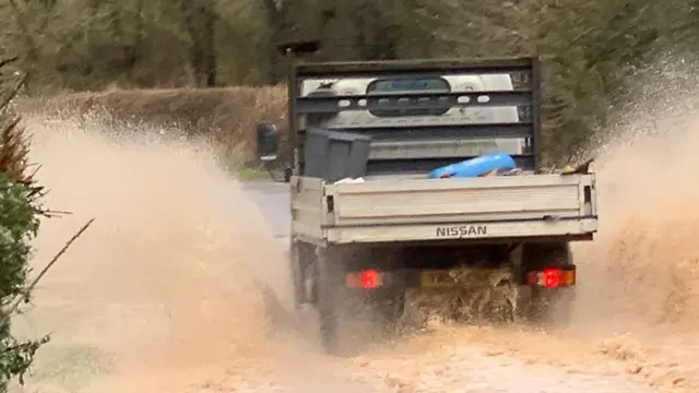 A vehicle drives through a flooded route in Southam