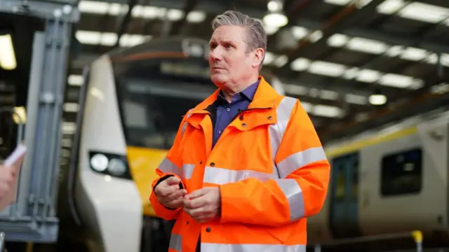 Labour leader Sir Keir Starmer speaks to the media and wears an orange safety jacket