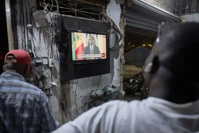 People watch Senegal's President Macky Sall during a live press conference broadcast on the national television, in the district of Medina in Dakar on February 22, 2024.