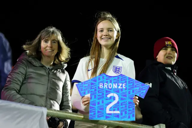 A fan holds a sig depciting a 'Bronze 2' England away shirt.