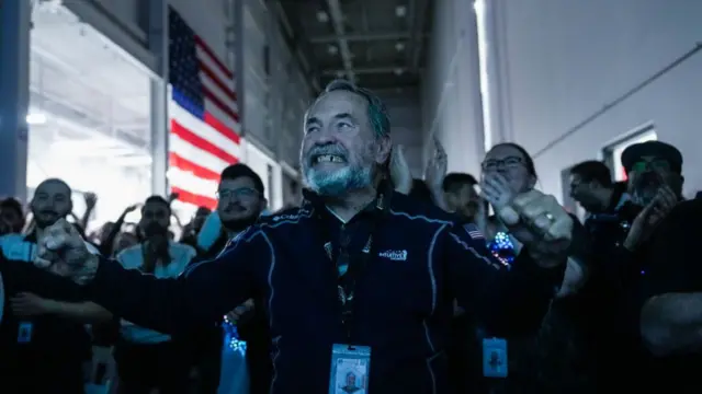 Dan Harrison clenching his fists and smiling in celebration, as colleagues clap behind him