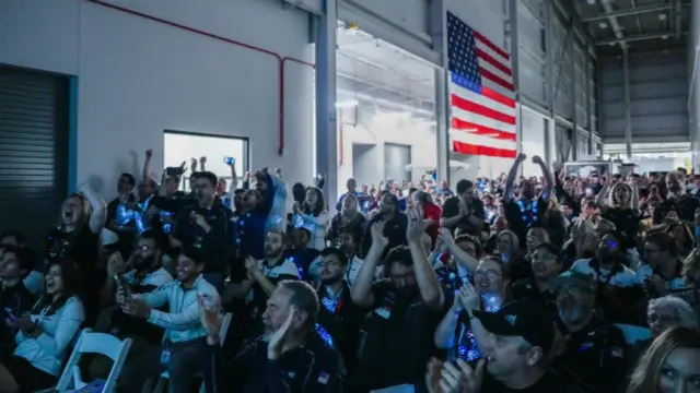 Intuitive Machines employees gathered raise their hands, clap and cheer