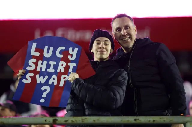 A fan holds up a Barcelona shirt sign with 'Bronze swap shirt?' on it.