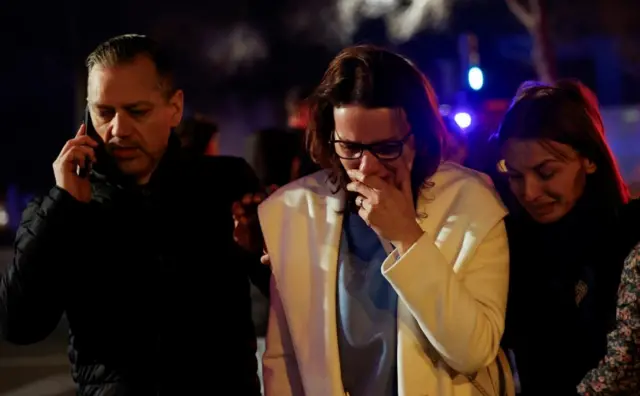 Three people, visibly upset, outside the fire-damaged building in Valencia