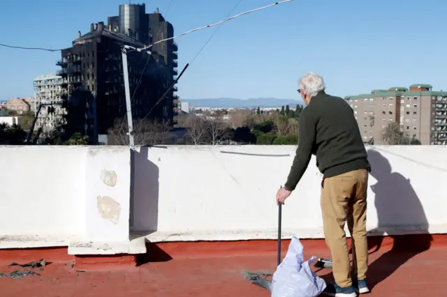 A man looks at the multi-storey residential block ravaged yesterday by a huge fire, killing at least four people, as he cleans ash on his rooftop terrace in Valencia on February 23, 2024.