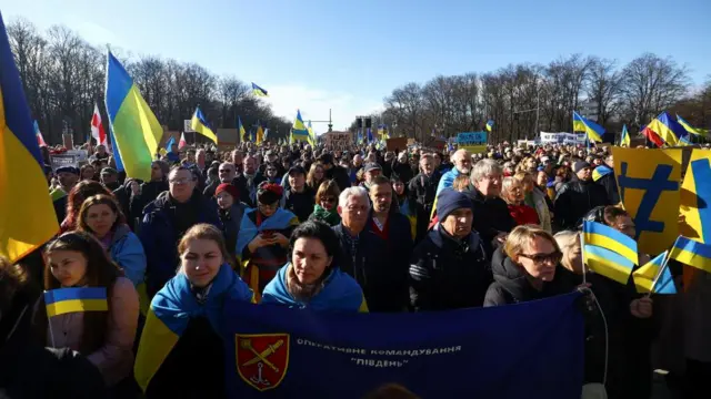 A crowd of demonstrators carrying Ukrainian flags march down a Berlin street