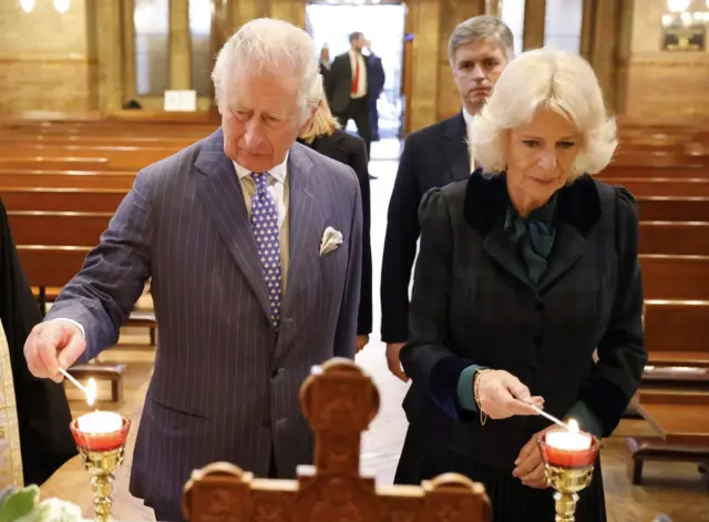 Charles and Camilla stand next to each other in a church and light candles on the alter