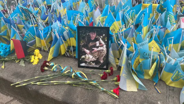 Roses in front of a picture of a soldier and Ukrainian flags