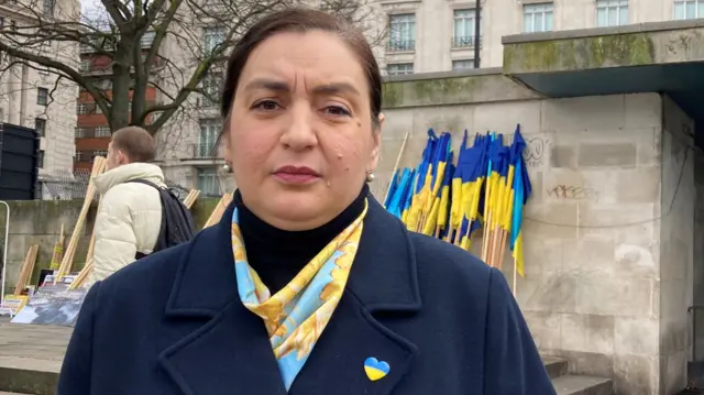 Natalia Ravlyuk, wearing a Ukraine flag pin badge and a blue and yellow scarf, stands in front of Marble Arch underground station