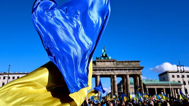 A Ukrainian national flag flutters as people gather in front of the Brandenburg Gate