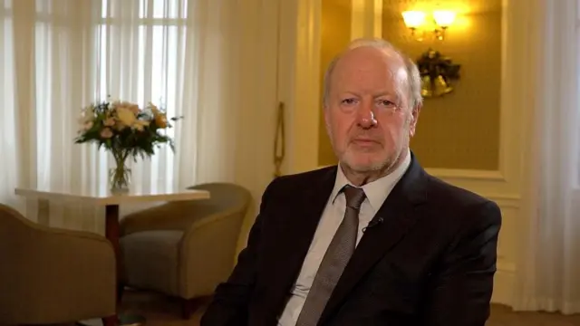 Alan Bates wearing a suit and tie during a BBC interview