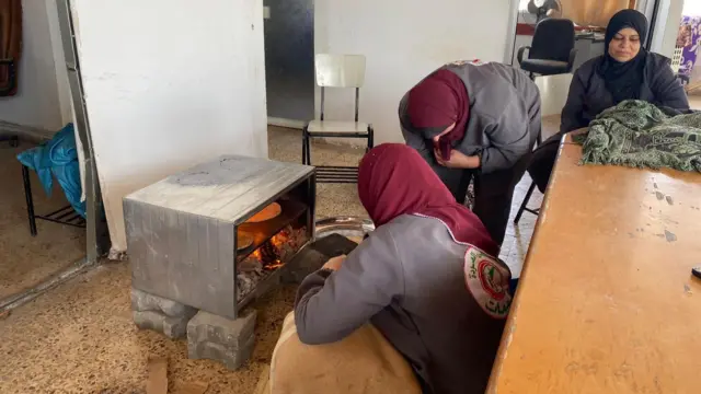 Hospital staff cook bread over a flame in a makeshift oven standing on bricks