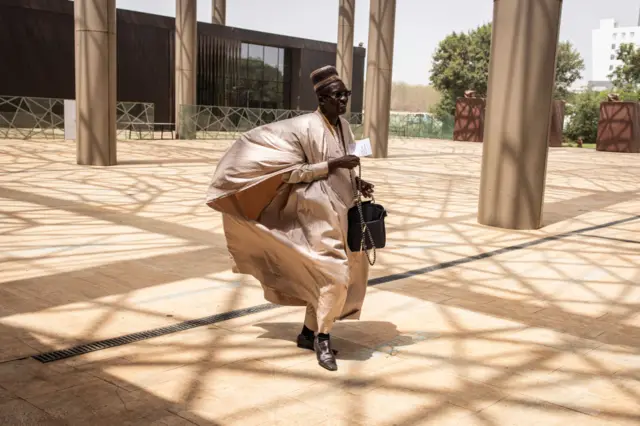 A delegate arrives in a large boubou that is being blown by the wind.