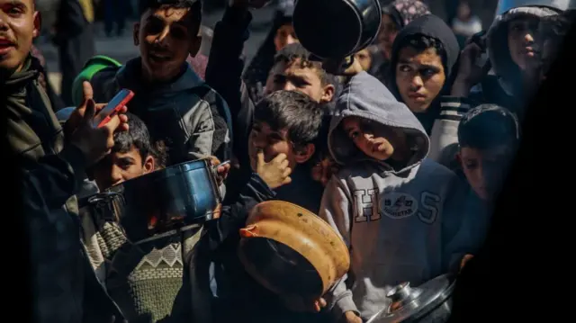 a dozen or so children are visible in frame, crowded together, all holding bowls