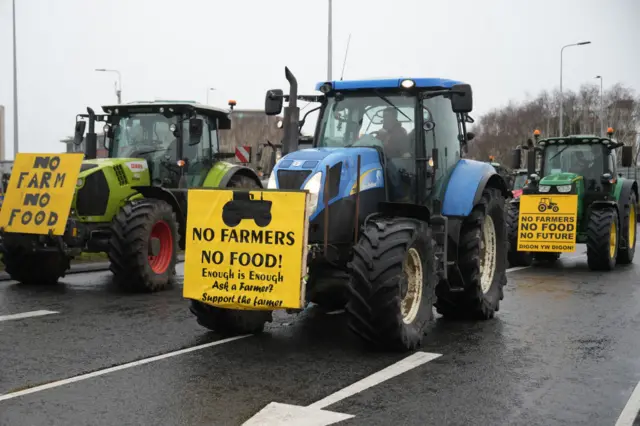 Tractors with signs reading "No Farmers No Food!" arrive at a holding area at the Queens Gate traffic Roundabout on February 28, 2024 in Cardiff, Wales