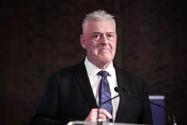 An image showing MP Lee Anderson in a suit, standing behind a microphone