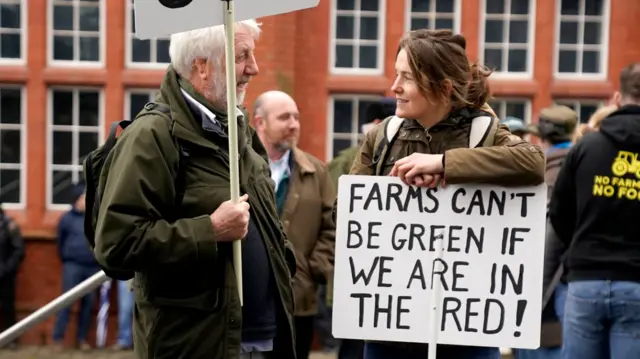 Farmers stand outside Senedd with sign that reads "Farms can't be green if we are in the red"