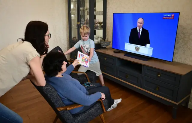 A family watches a TV broadcast of Russian President Vladimir Putin's annual state of the nation address in Moscow