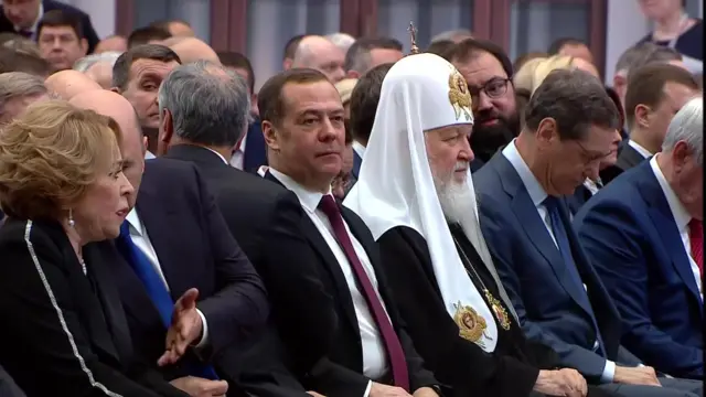 Figures gather in the hall where Putin is due to speak