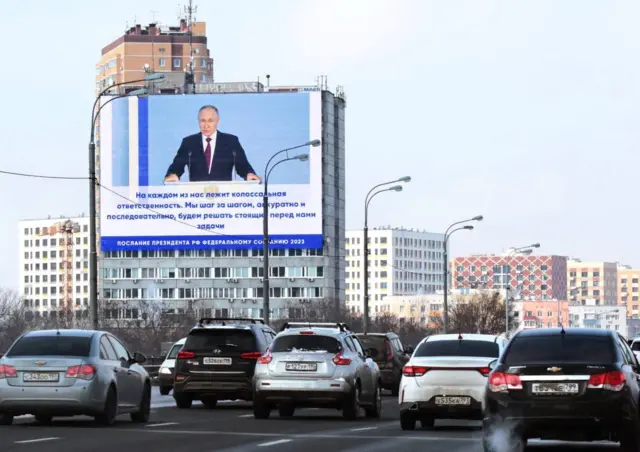 Large screens showing Putin's address